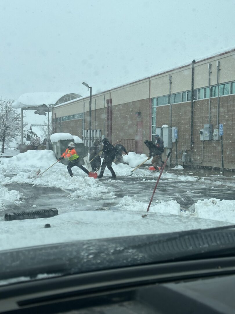 A group of people shoveling snow in front of a building.